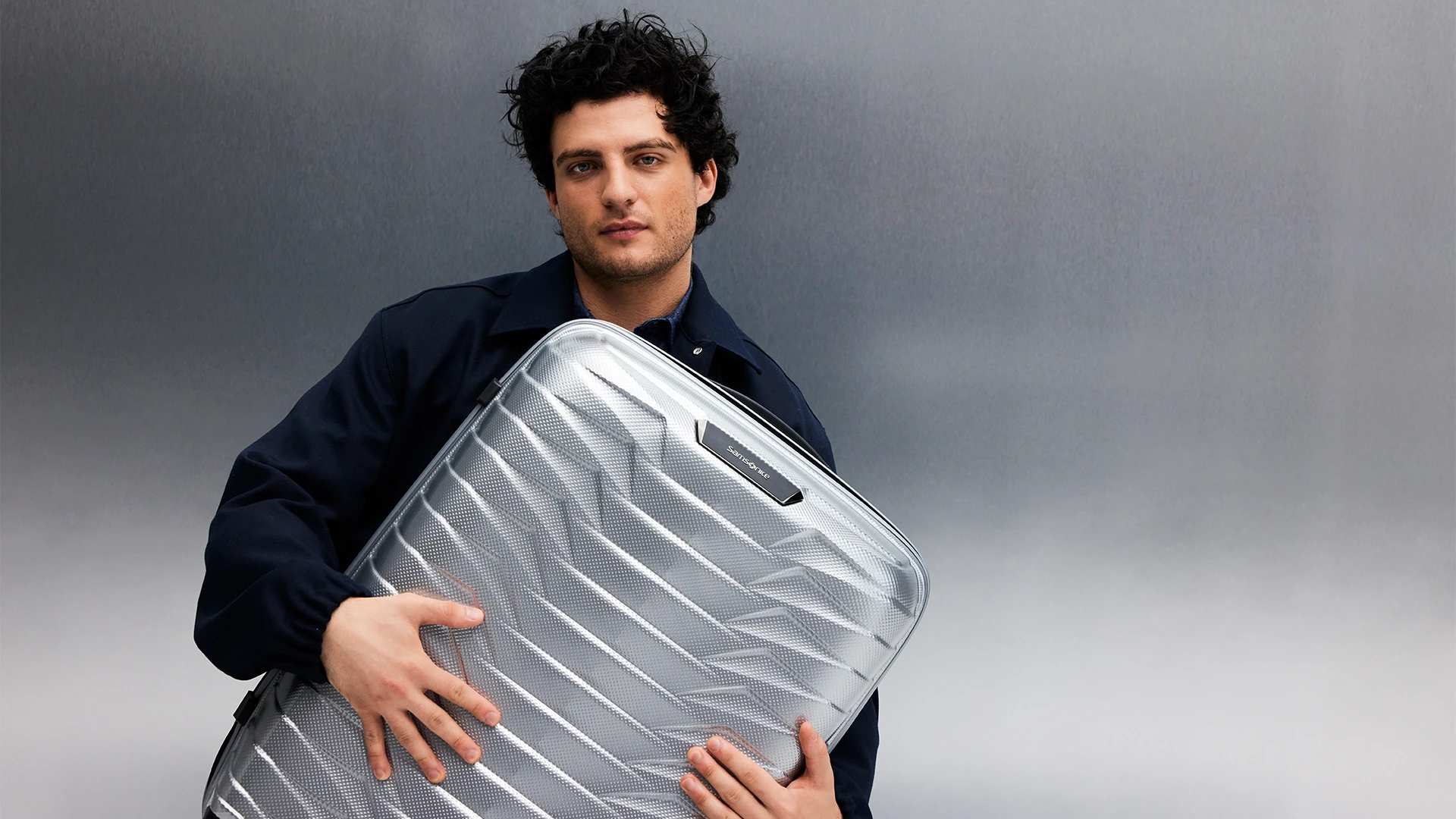 A young man with a Samsonite Proxis suitcase in a studio.