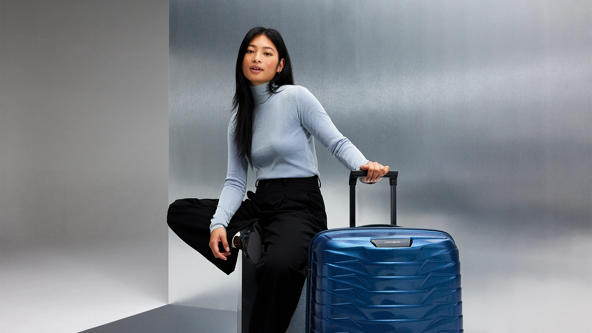 A young woman with a Samsonite Proxis suitcase in a studio.