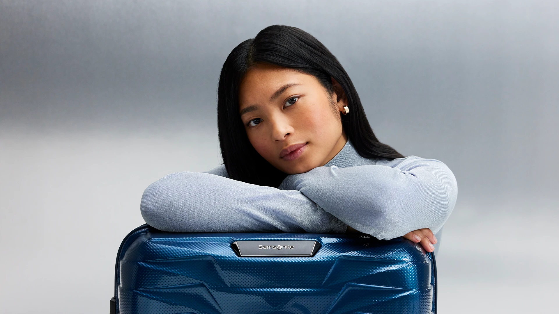 A young woman with a Samsonite Proxis suitcase in a studio.